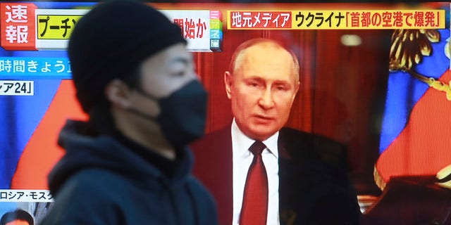 A man walks past a TV screen with image of Russia's President Vladimir Putin in Tokyo, Thursday, Feb. 24, 2022.