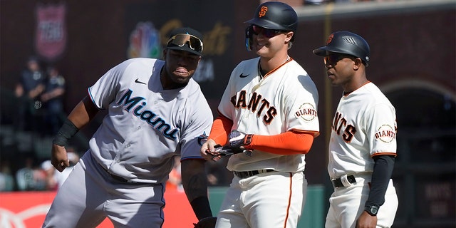 Miami Marlins first baseman Jesus Aguilar, left, congratulates San Francisco Giants' Joc Pederson, middle, after his base hit during the ninth inning of a game in San Francisco April 9, 2022. At right is Giants first base coach Antoan Richardson.