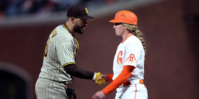 San Diego Padres first baseman Eric Hosmer, left, shakes hands with San Francisco Giants first base coach Alyssa Nakken during the third inning of a baseball game in San Francisco, Tuesday, April 12, 2022.