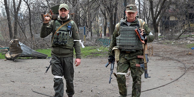 Armed servicemen of Donetsk People's Republic militia look at a photographer as they carry captured weapons in an area controlled by Russian-backed separatist forces in Mariupol, Ukraine, Friday, April 15, 2022. Mariupol, a strategic port on the Sea of Azov, has been besieged by Russian troops and forces from self-proclaimed separatist areas in eastern Ukraine for more than six weeks. 