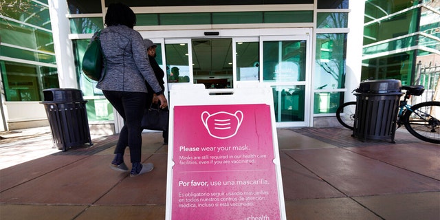 A sign advising visitors to don face coverings stands outside the main entrance to UCHealth University of Colorado hospital Friday, April 1, 2022, in Aurora, Colo. 