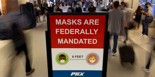 FILE PHOTO: Air travelers make their way past a sign mandating face masks for all during the outbreak of the coronavirus disease (COVID-19) at Phoenix international airport in Phoenix, Arizona, U.S. September 24, 2021. REUTERS/Mike Blake