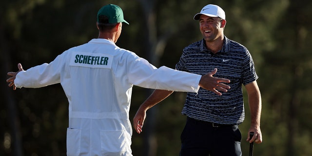 Scottie Scheffler and caddie Ted Scott celebrate on the 18th green after winning the Masters on April 10, 2022.