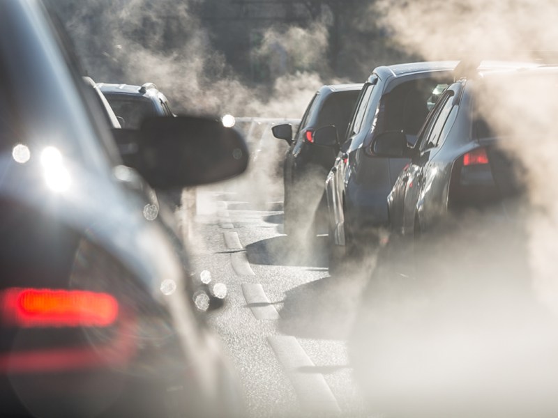 Blurred silhouettes of cars surrounded by steam from the exhaust pipes in a traffic jam. (LanaElcova via Shutterstock)