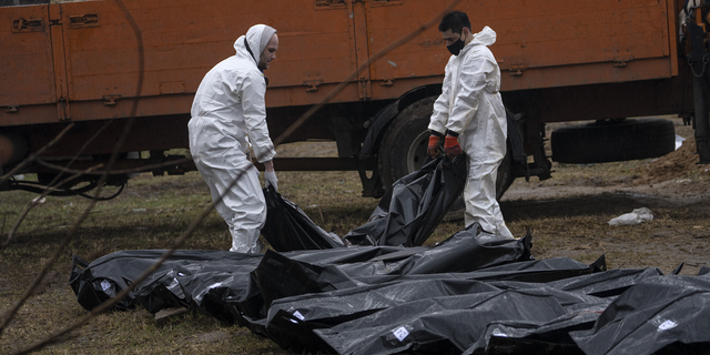 WARNING: GRAPHIC IMAGE: Cemetery workers carry a corpse of a man from a mass grave to be identified in a morgue in Bucha on Sunday.