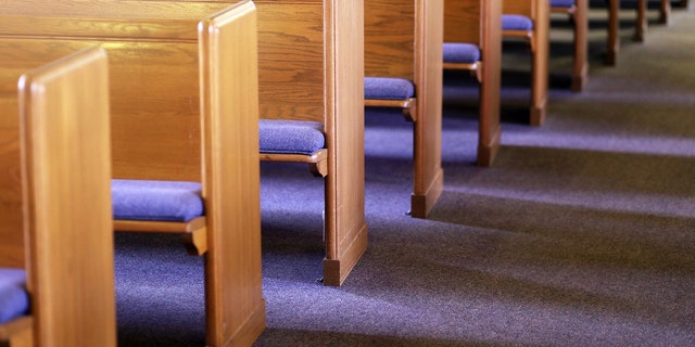 Window light is shining on rows of empty church pews in a church sanctuary.