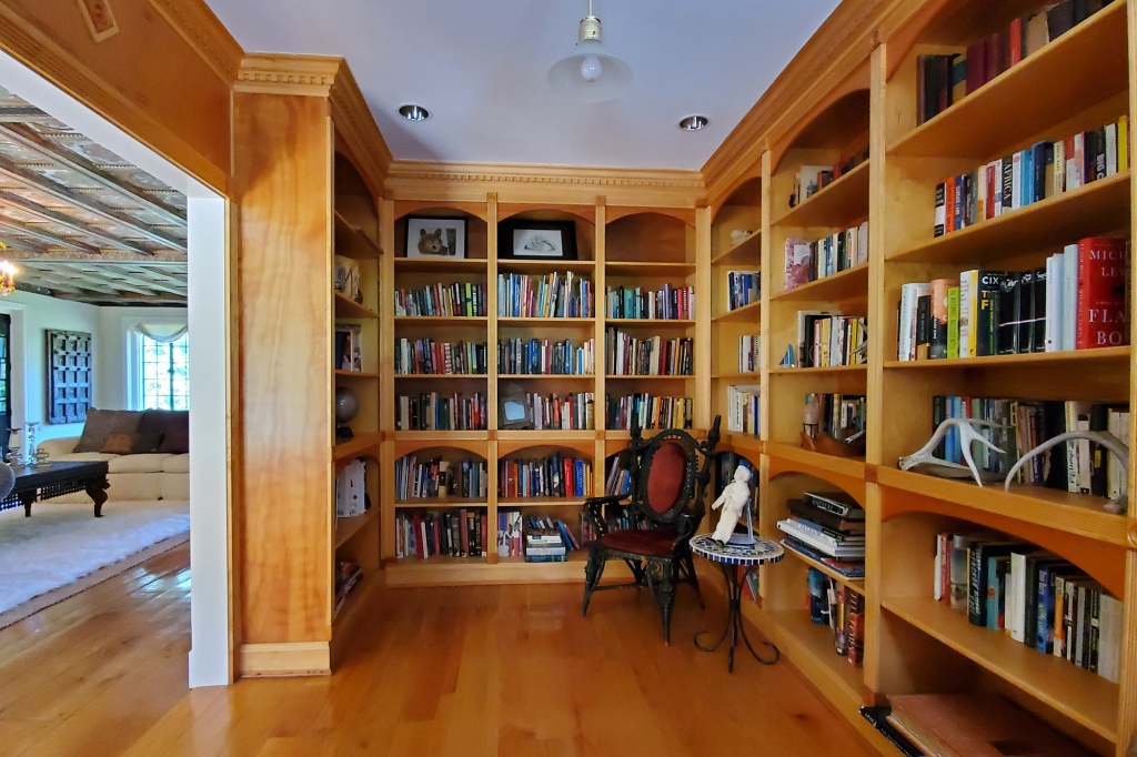 A library with built-in shelves stands next to the living area.