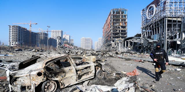 A police officer stands guard next to the Wreckage and debris outside a damaged shopping centre in the Podilskyi district of Kyiv by Russian air strikes, amid Russian invasion, in Kyiv, Ukraine, 21 March 2022. Russian invasions have forced millions of Ukrainians to become refugees fleeing to other countries.  (Photo by Ceng Shou Yi/NurPhoto via Getty Images)