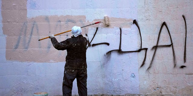 A worker paints over graffiti saying "Yes to Peace!" on the wall of an apartment building in St. Petersburg, Russia, March 18, 2022.