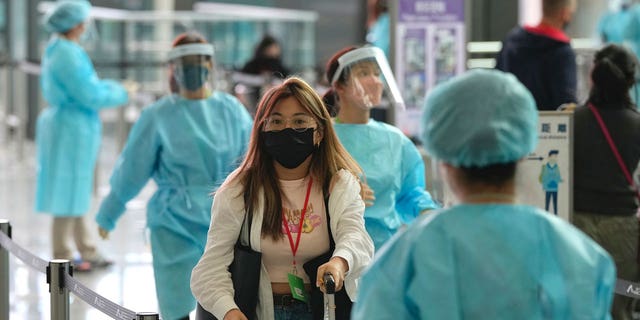 A worker in protective gear holds up a sign which reads "Do not crowd" as he directs a resident near a line for the first round of mass COVID testing in the Jingan district of western Shanghai, China, Friday, April 1, 2022. As residents of western Shanghai start a four day lockdown for mass testing, some in eastern Shanghai about to end their lock down are being told they will be confined to their homes for at least 10 more days. It was the latest wrinkle in the lockdown of China's largest city as it struggles to eliminate an omicron-driven coronavirus outbreak under China's zero-COVID policy. (AP Photo/Chen Si)