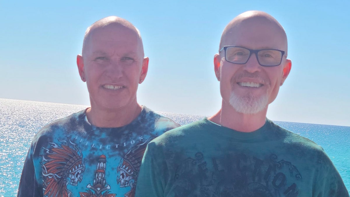 Herbert Swilley and Tim Smith pose together at the waterfront, backlit, wearing T-shirts