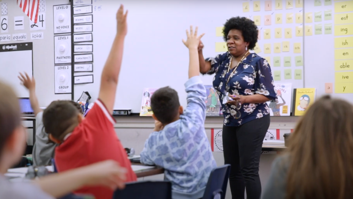 Students raising hands in front of teacher