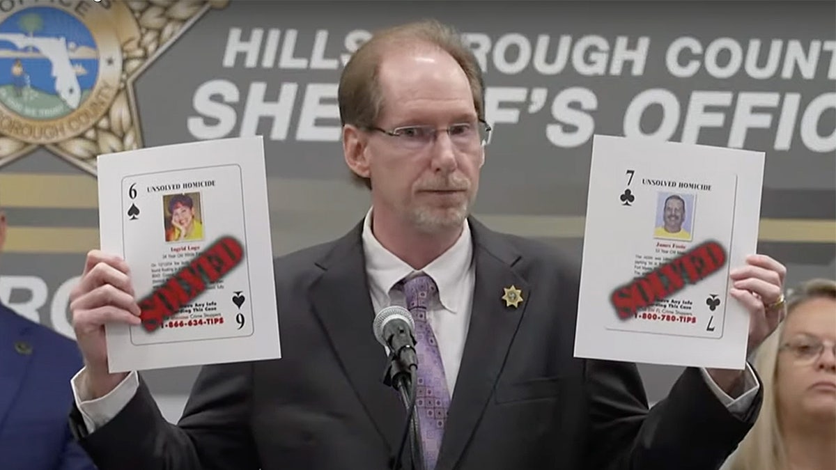 Joe Winkler holds up a pair of playing cards featuring homicide victims.