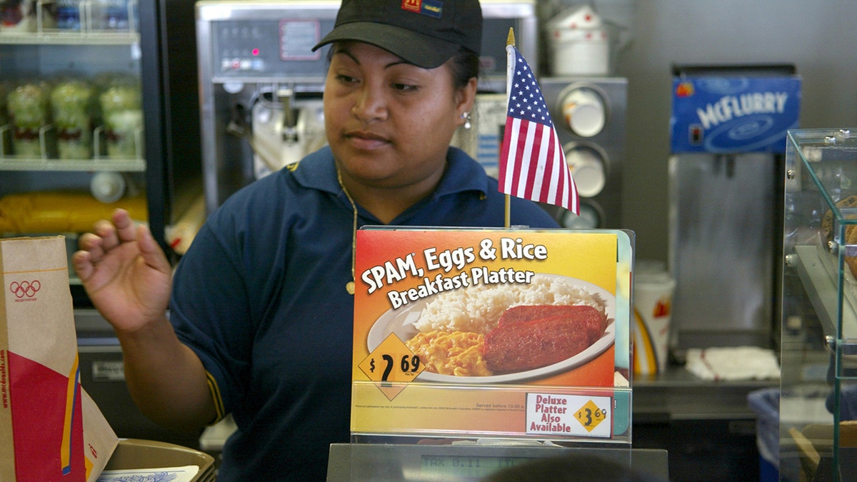 A cashier at a McDonald's location in Wahiawa, Hawaii, stands behind an advertisement for the then-new SPAM, Eggs and Rice Breakfast Platter in June 2002. Hawaii's residents consume more SPAM compared to residents of any other U.S. state.