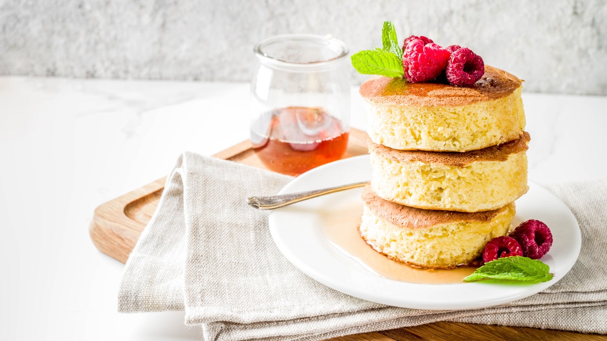 A plate of Japanese soufflé pancakes with maple syrup and raspberries is on display.