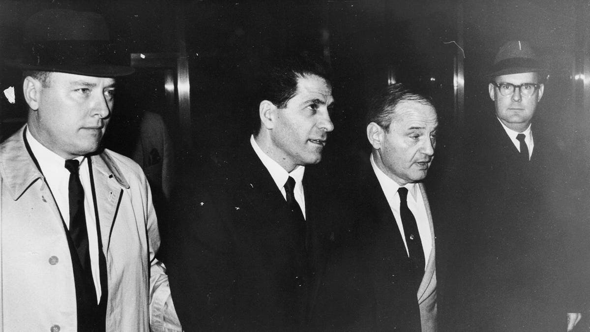 Sonny Franzese standing in between two men in suits looking serious.