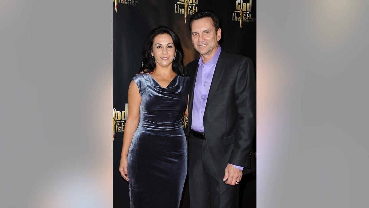 Michael Franzese in a grey suit and blue shirt next to his wife in a velvet aqua dress