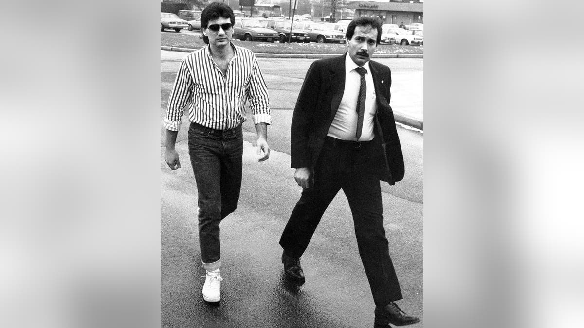 Michael Franzese in a striped shirt and glasses walking into court next to a man in a suit.