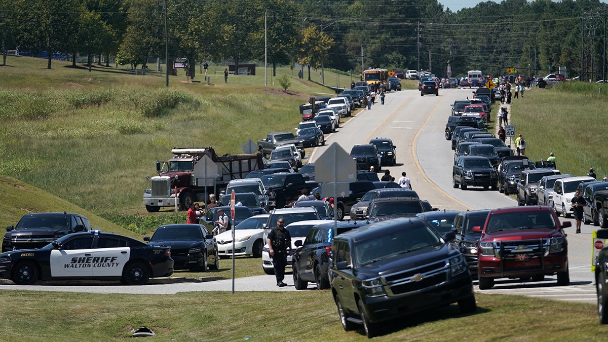 Cars are parked on the sides of a road as law enforcement officers work at the scene of a shooting at Apalachee High School