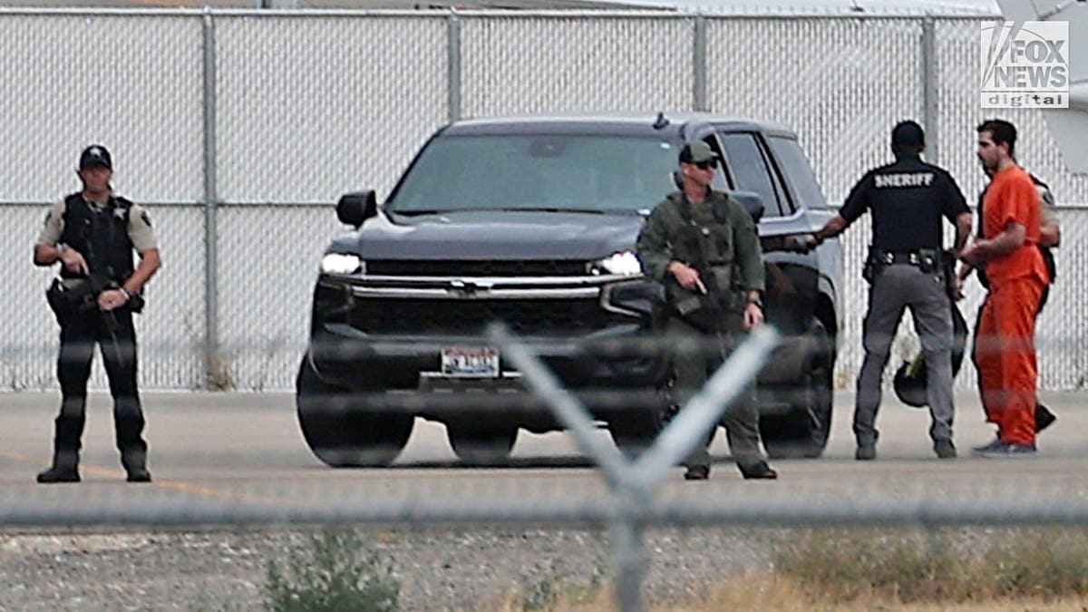 Bryan Kohberger in an orange prison jumpsuit ias led to a black SUV on an airport tarmac