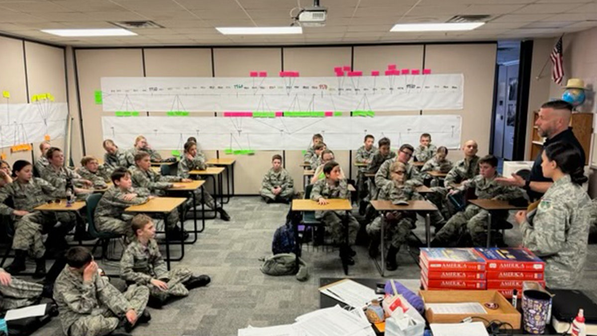 Students dressed in camouflage uniforms sit in classroom