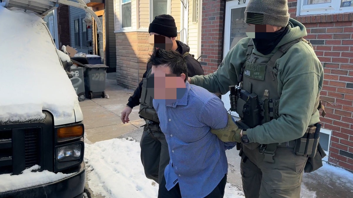 Two ICE officers lead away a man in handcuffs.