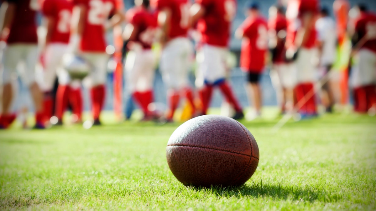 Close up of an american football on the field, players in the background