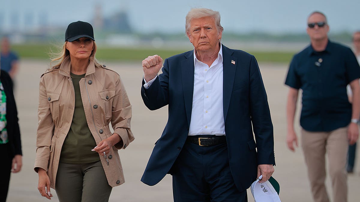 Donald Trump holds up a fist while walking with Melania Trump